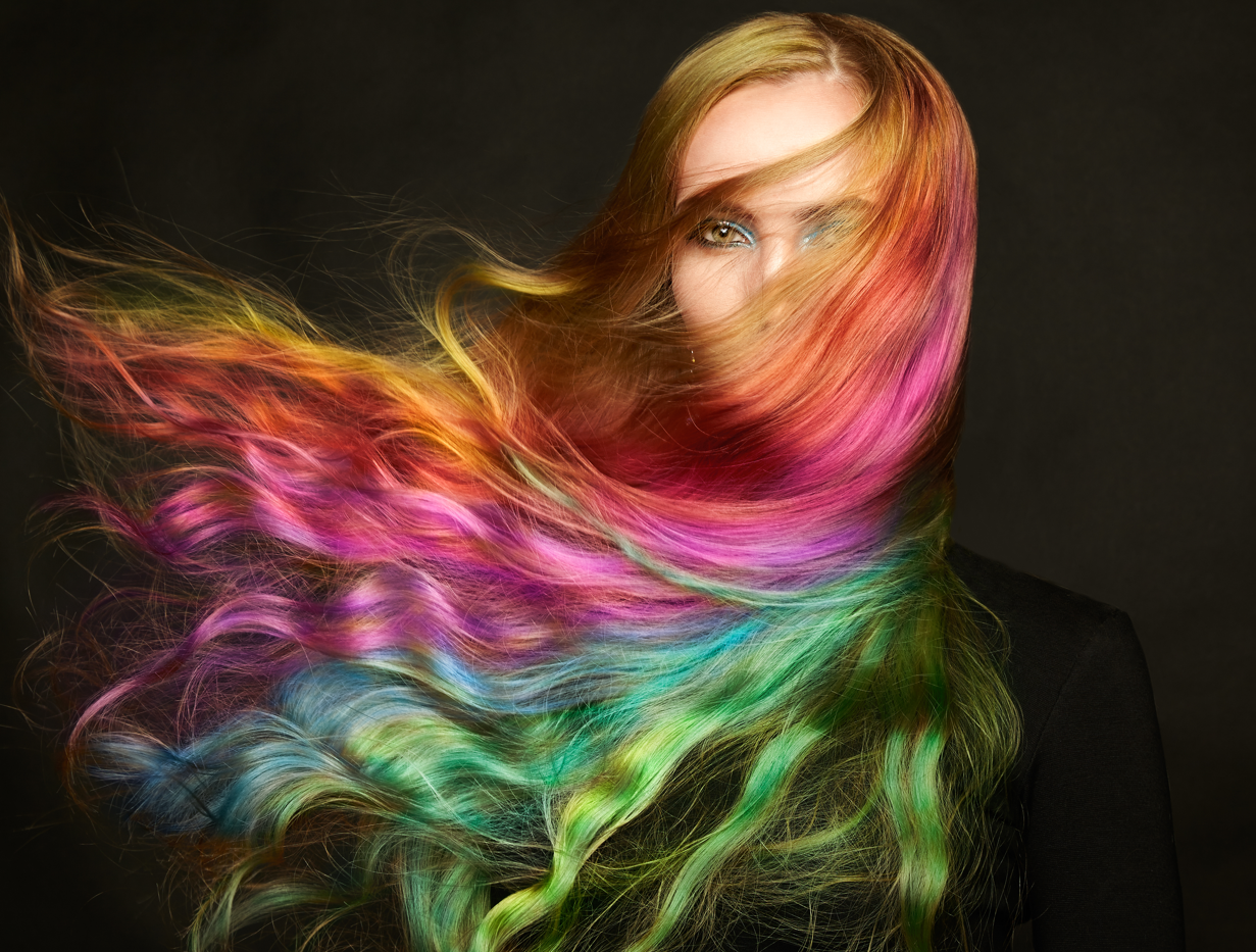 A woman with long flying hair with colourful dyes. Concept of rainbow coloured hair, hair dye, bleach, dyed hair. Dark background, face half hidden.