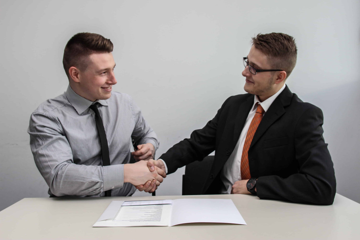 Two men shaking hands and expressing confidence during a job interview. 